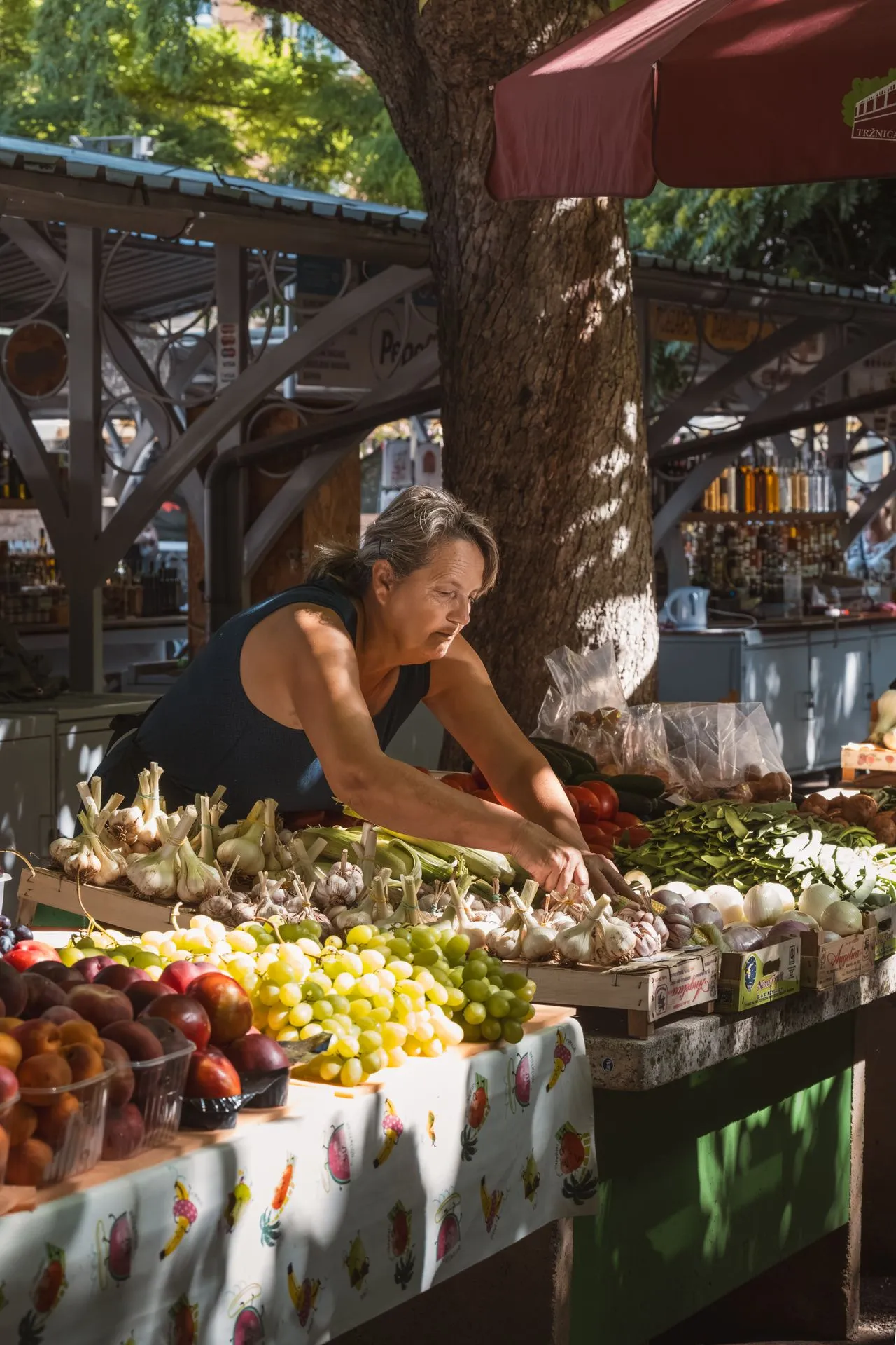 Woman arranging fresh fruit and vegetables on her outdoor stall at a Croatian market