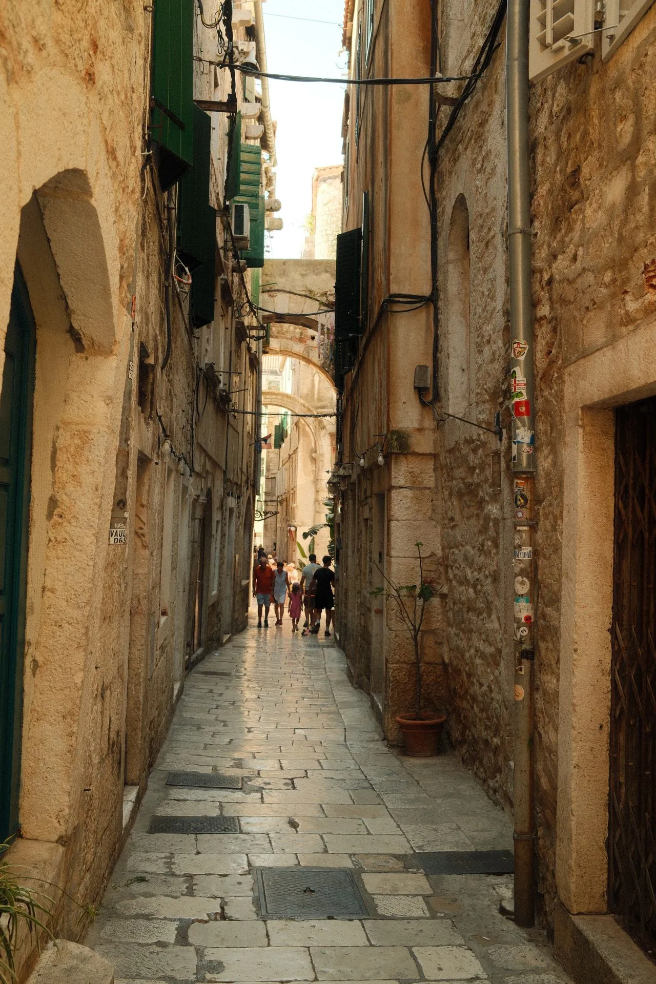 Narrow limestone lane in Split's old town with green shutters and a stone arch spanning the street